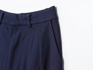 Detailed view of navy blue pleated trousers showing twill fabric and pocket stitching
