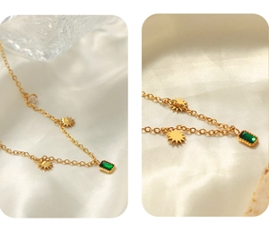 Close-up of gold-plated sun charm and green emerald rectangle pendant on necklace