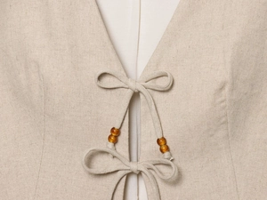 Macro detail of beige linen fabric with handcrafted tie-up and amber beaded accents