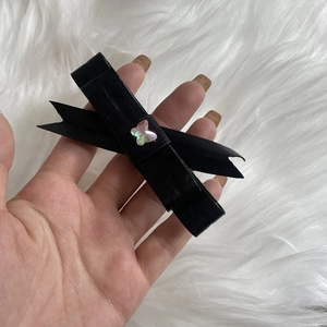 Detail view of a black leather bow hair clip with a butterfly charm held by hand