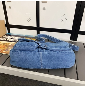 Détail du sac bandoulière en denim bleu montrant les coutures et la poche latérale