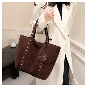 Detail of brown suede tote bag featuring metallic rivets and a heart-shaped charm
