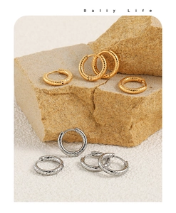 Detail of twisted gold and silver hoop earrings on a stone surface with soft lighting