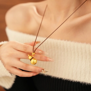 Brushed gold gourd pendant necklace with red accent on an elegant long rope chain