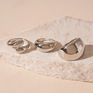 Three silver organic fluid metal rings displayed on a textured stone background