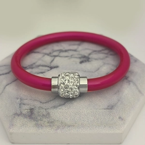 Detail eines rosenroten Silikonarmbands mit silbernem, kristallbesetztem Magnetanhänger