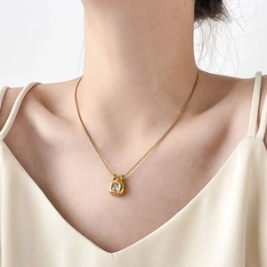 Close-up of gold necklace with square pendant and round zircon worn by model