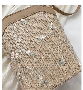 Gros plan détaillé du sac seau en paille avec broderie florale sur un tissu blanc doux
