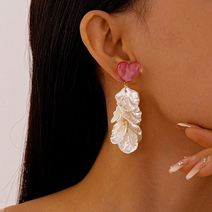 Détail de boucles d'oreilles cœur avec pompons de pétales blancs portés par mannequin