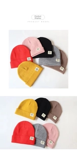 Close-up of baby knit beanies with smiley face patches in six vibrant colors
