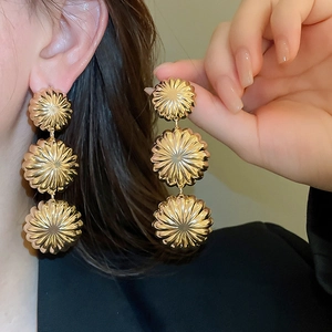 Detail of gold triple-tiered sunburst drop earrings on model showcasing metallic texture