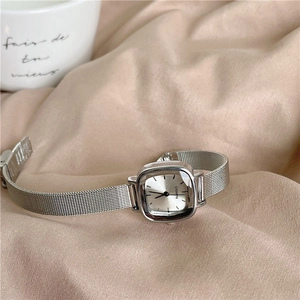Detail view of square silver lady watch with metal mesh strap on beige fabric background