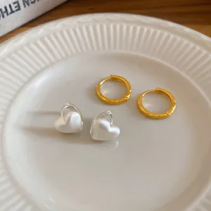 Minimalist heart pendant earrings and textured gold hoops on an elegant ceramic plate