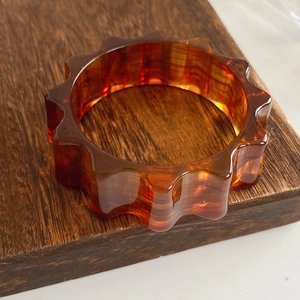 Macro shot of an amber resin bangle with unique gear-shaped edges on dark wood surface
