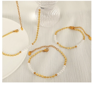 Detailed close-up of a gold pearl necklace with lobster clasp on white fabric