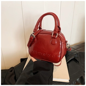 Detail of red patent leather handbag with embossed lettering and curved handles