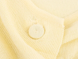 Close-up of knit fabric texture and matching fabric-covered button on a cream yellow top