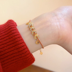 Détail du bracelet corde rouge tressée plaqué or avec cinq breloques pièces serties