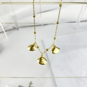 Detail of gold seashell pendants on a beaded stainless steel chain over marble