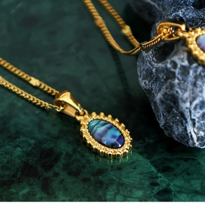 Macro view of oval abalone shell pendants on gold snake chains against dark marble