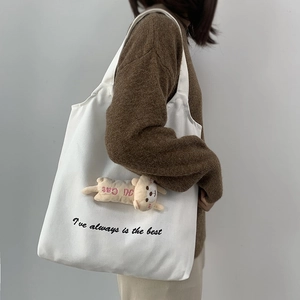 Detail of white canvas tote bag with lettering and cute plush cat pendant hanging on side