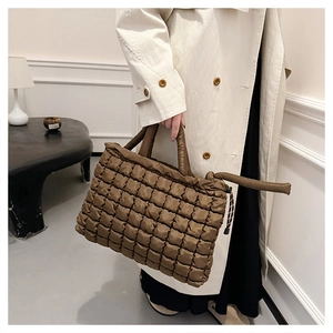 Close-up of brown quilted down cotton tote bag with handle held by a model