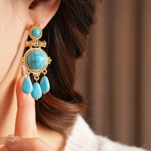 Close-up of vintage gold earrings with turquoise-style stones and waterdrop charms