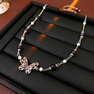 Close-up of gold chain bracelet with purple butterfly charm and white pearls on black tray