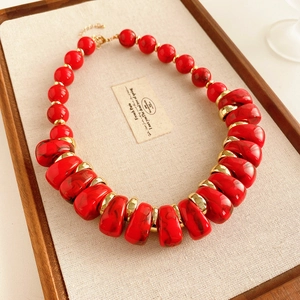 Détail d'un collier vintage rouge perlé avec des séparateurs dorés sur un plateau
