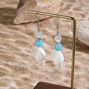 Close-up of shell drop earrings with turquoise beads on a sand beach background