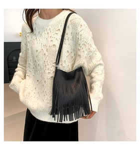 Detail of black pebbled leather crossbody bag with long tassels on a white knit sweater