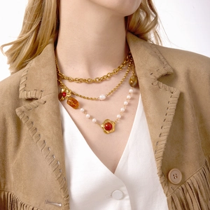 Dettaglio di una collana a strati dorata con perle e ciondolo a fiore rosso su modella
