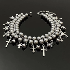 Macro view of multi-layer silver beaded bracelet with cross and bell charms on dark surface