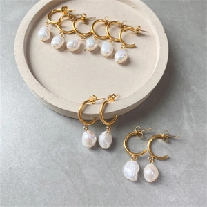 Macro detail of golden stainless steel hoop earrings with natural baroque pearl pendants