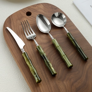 Modern 4-piece stainless steel cutlery set with green bamboo-style handles on wood