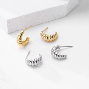 Macro shot of minimalist gold and silver croissant twist earrings on white stone block