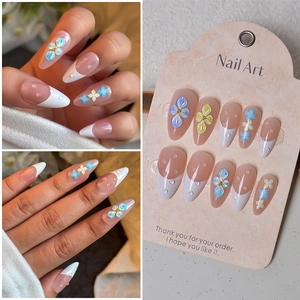 Detail of almond-shaped nude press-on nails with white French tips and 3D floral accents
