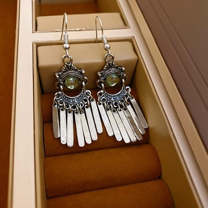 Close-up of vintage silver phoenix crescent earrings with green stones and fringe