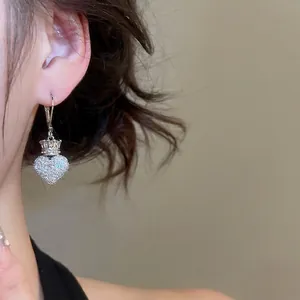Elegant silver heart and crown earrings encrusted with zircon crystals on a female model