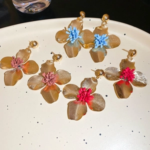 Detailed close-up of colorful flower petal earrings in gold, blue and red on a ceramic plate