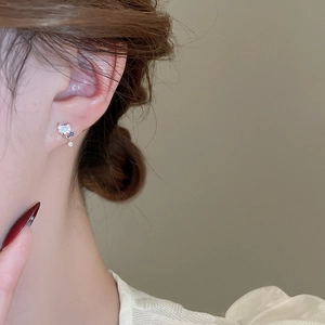 Detail of heart-shaped zircon earrings with tiny blue stone on a female model