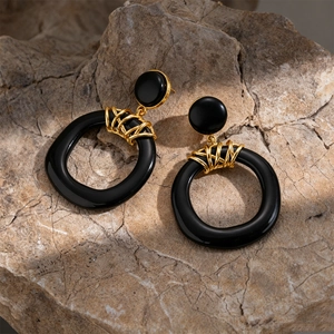 Detail of black resin geometric earrings with gold wire wrap on a textured rock surface