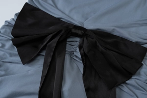 Detail of blue dress featuring a large black satin bow and elegant ruching textures