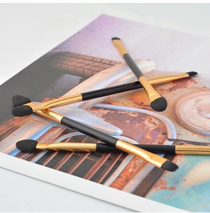 Close-up of double-ended eyeshadow brushes with black handles and gold ferrules on a desk