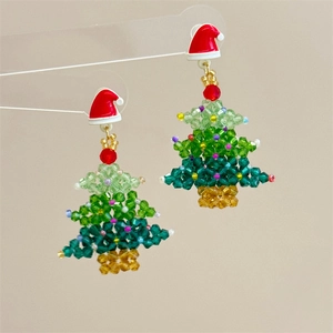 Macro detail of handmade beaded Christmas tree earrings with a red enamel hat top