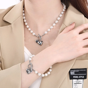 Close-up of pearl necklace and bracelet set with silver heart charms on female model
