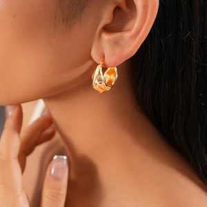 Gros plan d'une boucle d'oreille créole dorée ondulée portée par un mannequin