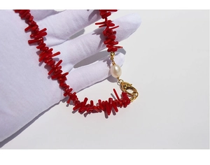 Macro detail of red branch-style necklace featuring a white pearl and gold clasp fastener