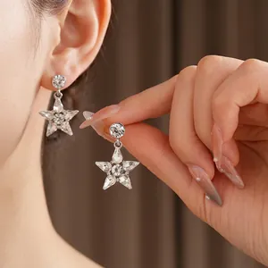 Star shaped silver studs with crystals shown on ear and held by fingers