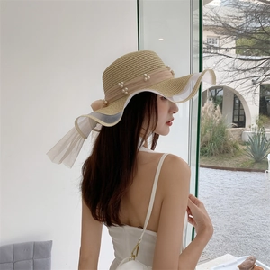Detailed view of khaki straw hat with elegant white pearls and mesh bow decoration